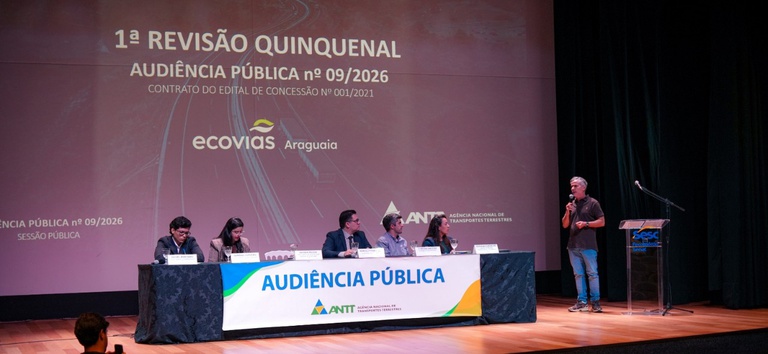 IMAGEM DO AUDITORIO COM 5 PESSOS ATRAS DA MESA